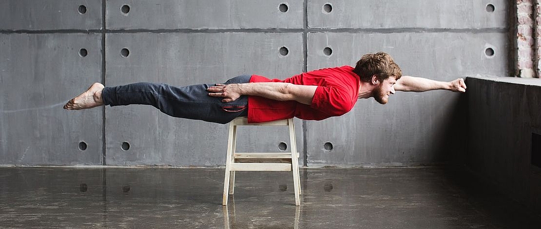 Ein junger Mann liegt quer auf einem Hocker und posiert als Superheld. 