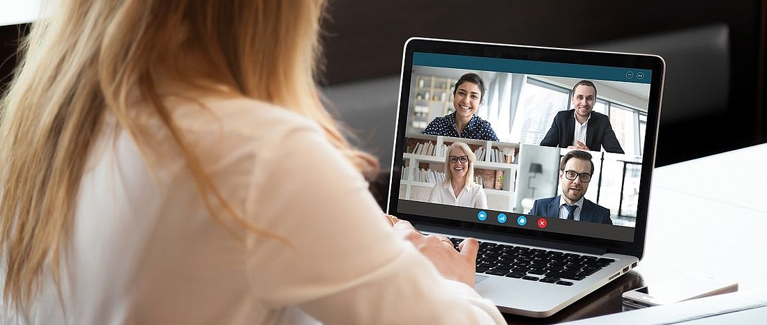 Eine junge Frau sitzt am Laptop und hält mit weiteren vier Personen eine Videokonferenz ab.