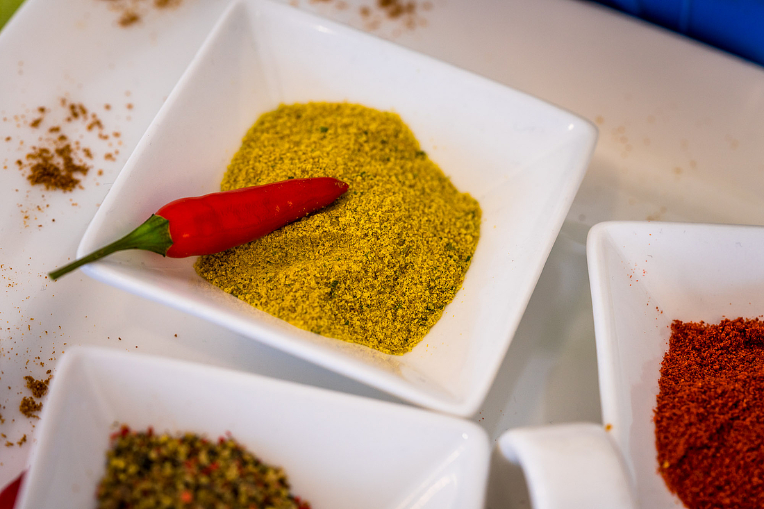 Eine Schale mit Currypulver steht auf einem Tisch. Auf dem Currypulver liegt eine rote Chilischote.