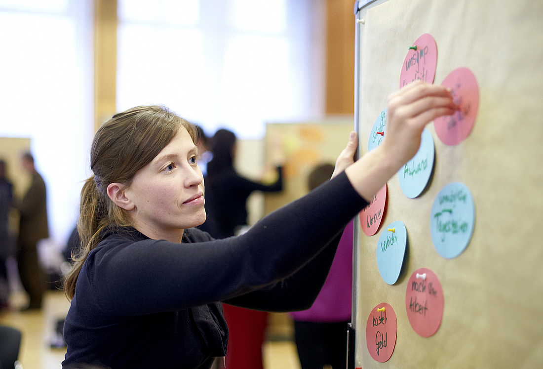 Eine junge Frau befestigt Kärtchen mit den Diskussionsergebnissen an einer Pinnwand.