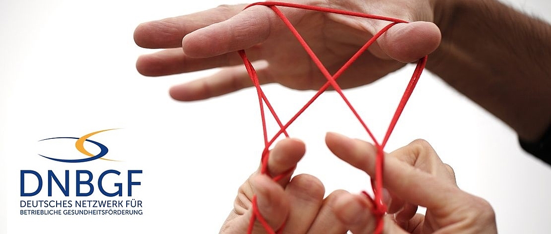 Zwei Personen spielen ein Fadenspiels mit einem roten Faden. Nahaufnahme der Hände.