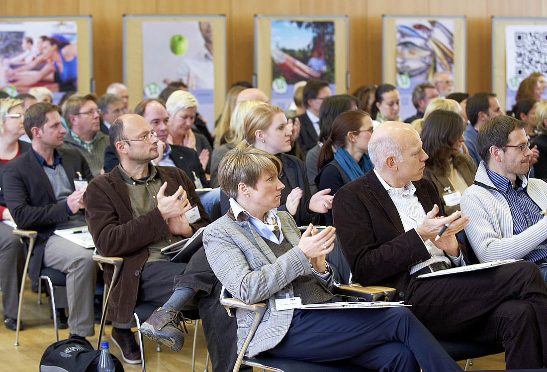 Publikum sitzt im Veranstaltungssaal und applaudiert.