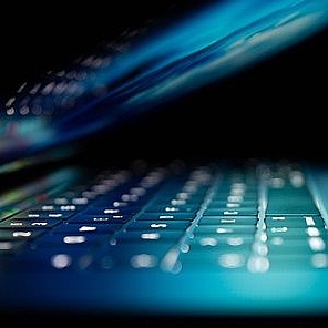 Ein Laptop ist zur Hälfte zugeklappt. Die Tastatur leuchtet intensiv.