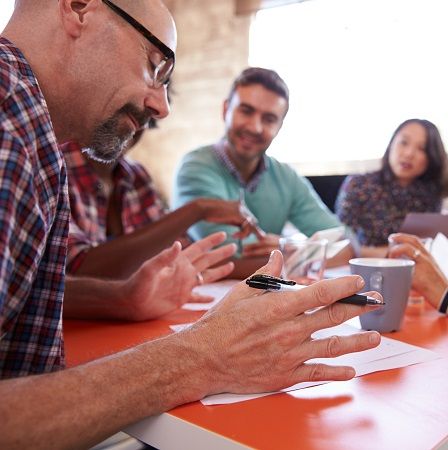 Ein Mann sitzt an einem Besprechungstisch und berät sich mit vier weiteren Männern und Frauen.