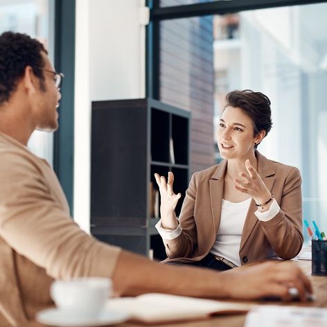 Titelbid des iga.Expertendialogs 2024: Zwei Mitglieder eines Teams, ein Mann und eine Frau, sitzen beisammen im Büro und besprechen etwas bei einem Kaffee.