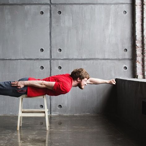 Ein junger Mann liegt quer auf einem Hocker und posiert als Superheld.