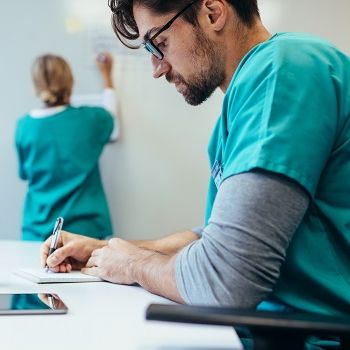 Ein Pfleger sitzt im Pausenraum und macht sich Notizen.