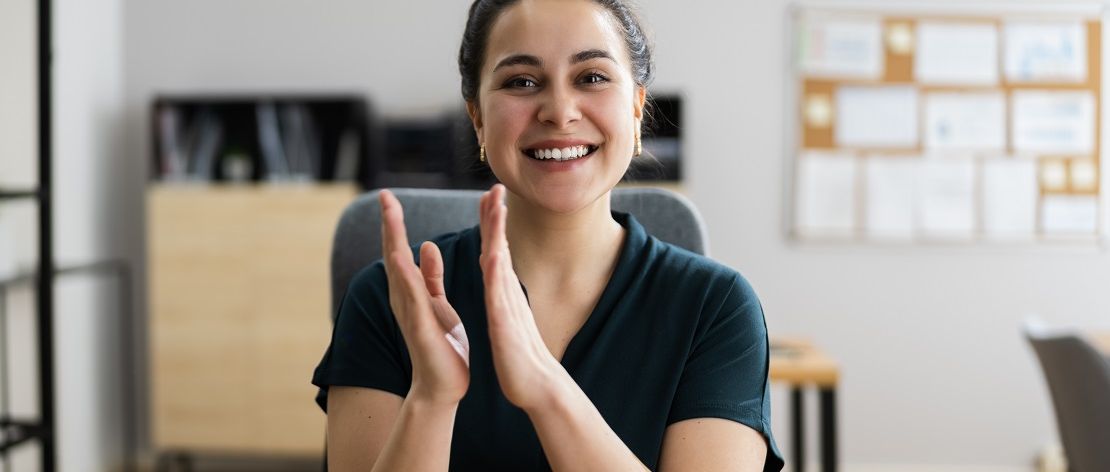 Eine junge Frau klatscht stolz in die Hände.