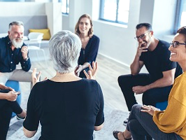 6 Personen sitzen in einem Stuhlkreis und diskutieren. Alle Beteiligten sind aufmerksam und fröhlich.