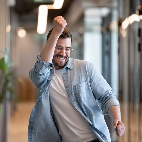 Ein Mann führt einen Freudentanz auf den Gang eines Bürotraktes auf. Als Siegespose ballt er seine Hände zu Fäusten.
